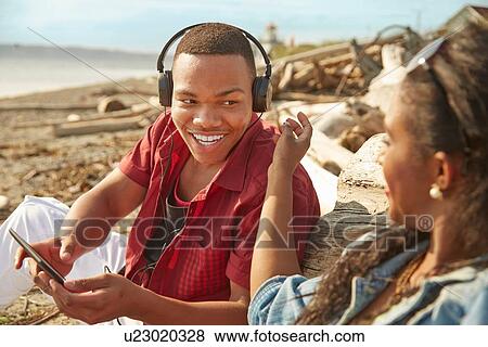 Young couple sitting on beach, man wearing headphones View Large Photo Image Stock Photo - Young couple sitting on beach, man wearing headphones. Fotosearch