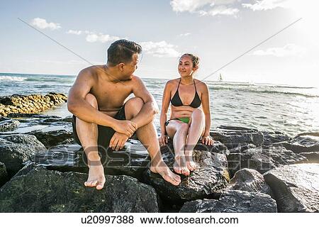 Stock Photo - Young couple sitting on rocks at Waikiki Beach, Hawaii, USA. Fotosearch