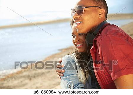 Young couple standing together on beach smiling, hugging looking away View Large Photo Image Picture - Young couple standing together on beach smiling, hugging looking away. Fotosearch