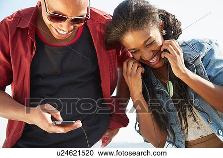 Young couple standing together side by side smiling using smartphone View Large Photo Image Stock Image - Young couple standing together side by side smiling using smartphone. Fotosearch