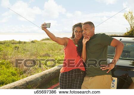 Stock Photograph - Young couple using smartphone, taking selfie, making faces. Fotosearch
