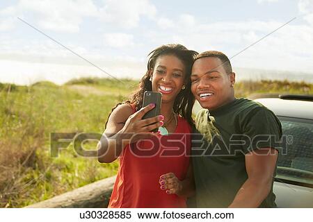 Young couple using smartphone, taking selfie View Large Photo Image Stock Photography - Young couple using smartphone, taking selfie. Fotosearch