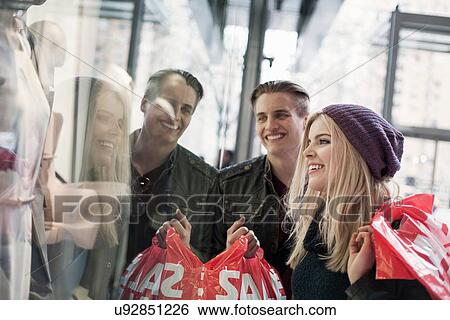Stock Photograph - Young couple window shopping with sale shopping bags, New York, USA. Fotosearch