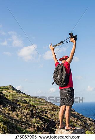 Stock Photography - Young male tourist holding up his digital SLR on Makapuu coast path, Oahu, Hawaii, USA. Fotosearch