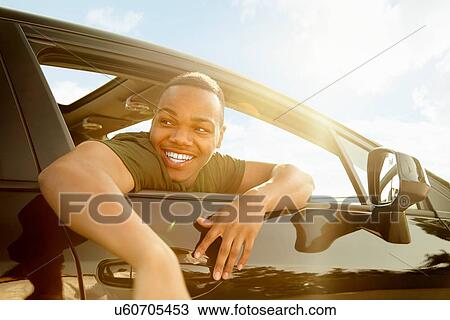 Stock Image - Young man leaning out of car window smiling. Fotosearch