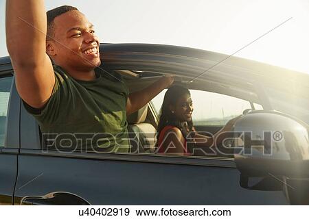 Young man leaning out of car window smiling, arms raised View Large Photo Image Stock Photo - Young man leaning out of car window smiling, arms raised. Fotosearch