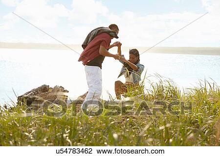 Stock Image - Young man lending a helping hand to young woman climbing. Fotosearch