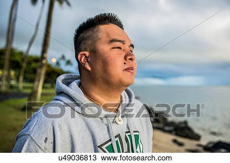 Stock Image - Young man looking out at sunrise from Kaaawa beach, Oahu, Hawaii, USA. Fotosearch