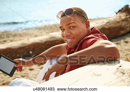 Young man on beach holding digital tablet, looking at camera View Large Photo Image Stock Image - Young man on beach holding digital tablet, looking at camera. Fotosearch