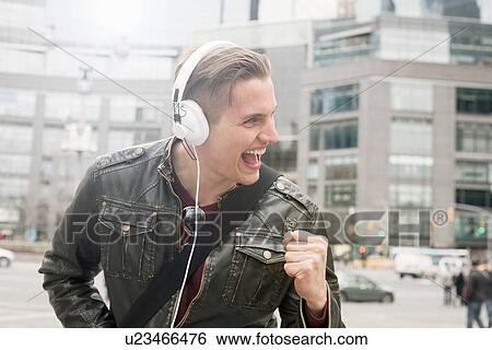 Young man on street listening to headphones with clenched fist, New York, USA View Large Photo Image Stock Photograph - Young man on street listening to headphones with clenched fist, New York, USA. Fotosearch