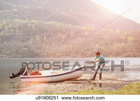 Stock Image - Young man pulling girlfriend in boat, Lake Mergozzo, Verbania, Piemonte, Italy. Fotosearch