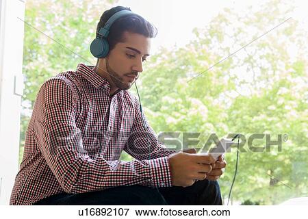 Young man selecting music on smartphone in cafe window seat View Large Photo Image Stock Photo - Young man selecting music on smartphone in cafe window seat. Fotosearch