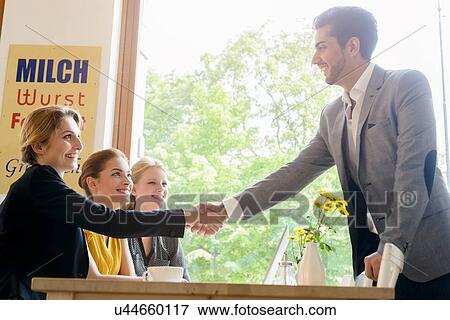 Young man shaking hands with young women in cafe View Large Photo Image Stock Photo - Young man shaking hands with young women in cafe. Fotosearch