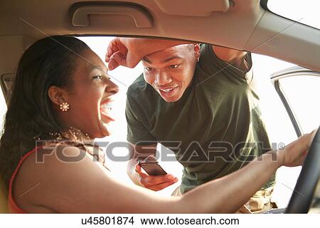Young man standing at open car door smiling at young woman View Large Photo Image Picture - Young man standing at open car door smiling at young woman. Fotosearch