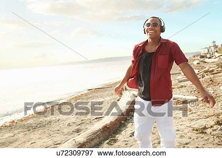 Stock Photo - Young man standing on beach wearing headphones and sunglasses. Fotosearch