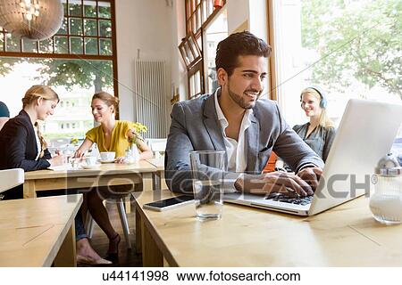 Stock Photo - Young man using laptop in cafe. Fotosearch