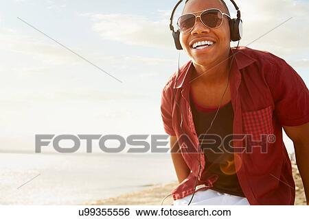 Young man wearing headphones and sunglasses, smiling looking at camera View Large Photo Image Stock Photograph - Young man wearing headphones and sunglasses, smiling looking at camera. Fotosearch