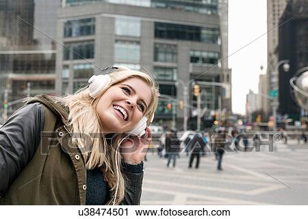 Stock Image - Young woman bending sideways whilst listening to headphones, New York, USA. Fotosearch