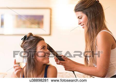 Stock Image - Young woman doing friend's hair. Fotosearch