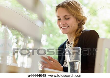 Stock Photo - Young woman in cafe reading texts on smartphone. Fotosearch