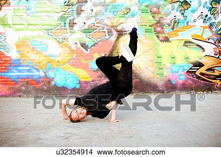 Picture - Young woman in upside down breakdancing freeze against graffiti. Fotosearch