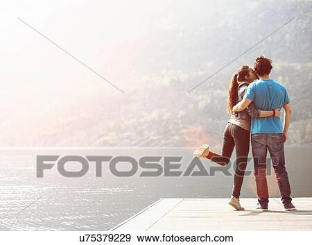 Stock Photo - Young woman kissing boyfriend on pier at Lake Mergozzo, Verbania, Piemonte, Italy. Fotosearch