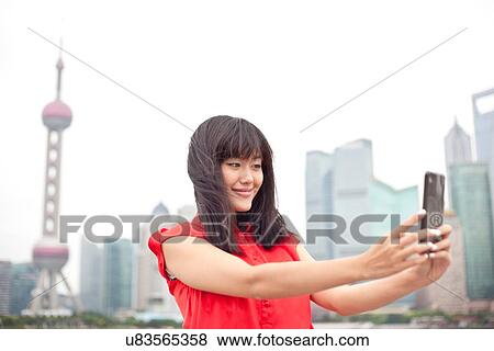 Stock Photo - Young woman looking at smartphone, outdoors, Shanghai, China. Fotosearch