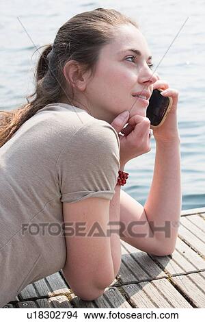 Young woman lying on pier chatting on smartphone, Lake Mergozzo, Verbania, Piemonte, Italy View Large Photo Image Picture - Young woman lying on pier chatting on smartphone, Lake Mergozzo, Verbania, Piemonte, Italy. Fotosearch