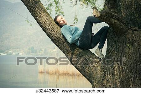 Stock Photo - Young woman reclining in tree on lakeside, Lake Mergozzo, Verbania, Piemonte, Italy. Fotosearch