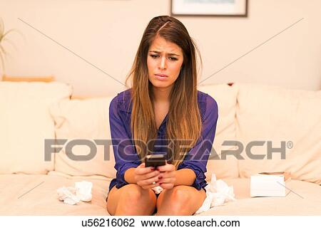 Young woman sitting on sofa, looking at smartphone with sad expression View Large Photo Image Stock Image - Young woman sitting on sofa, looking at smartphone with sad expression. Fotosearch