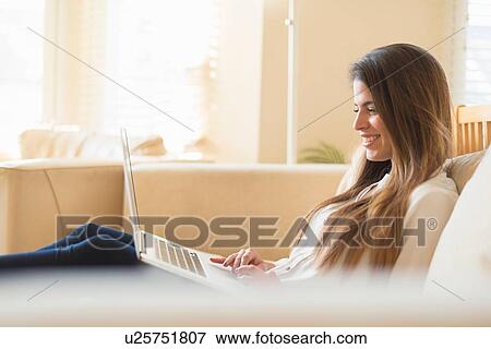 Young woman sitting on sofa, using laptop View Large Photo Image Stock Photo - Young woman sitting on sofa, using laptop. Fotosearch