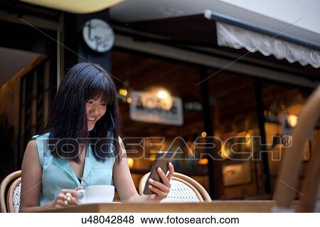 Young woman, sitting outside cafe, using smartphone, Shanghai, China View Large Photo Image Stock Photo - Young woman, sitting outside cafe, using smartphone, Shanghai, China. Fotosearch