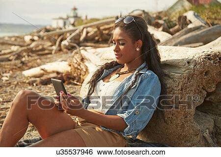 Young woman sitting relaxing on beach using digital tablet View Large Photo Image Stock Photograph - Young woman sitting relaxing on beach using digital tablet. Fotosearch