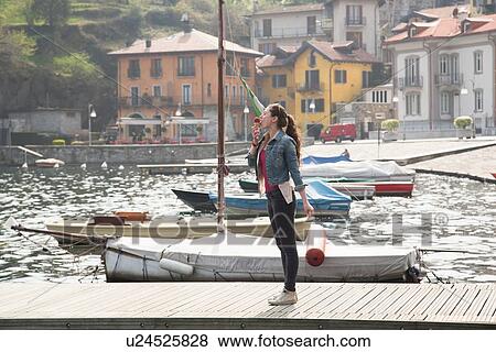 Young woman standing on pier eating ice cream cone at lake Mergozzo, Verbania, Piemonte, Italy View Large Photo Image Stock Photo - Young woman standing on pier eating ice cream cone at lake Mergozzo, Verbania, Piemonte, Italy. Fotosearch
