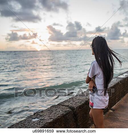 Stock Photo - Young woman watching sunrise, Kaaawa beach, Oahu, Hawaii, USA. Fotosearch