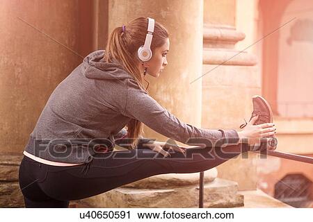 Young woman wearing sports clothes and headphones stretching legs View Large Photo Image Stock Image - Young woman wearing sports clothes and headphones stretching legs. Fotosearch
