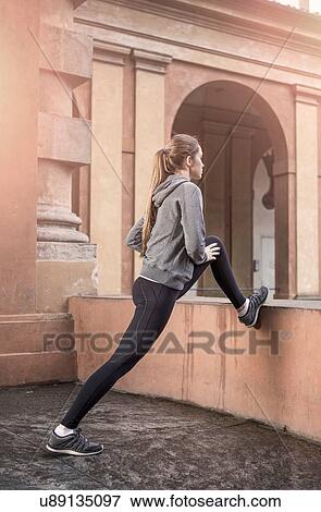 Stock Photo - Young woman wearing sports clothes stretching legs. Fotosearch