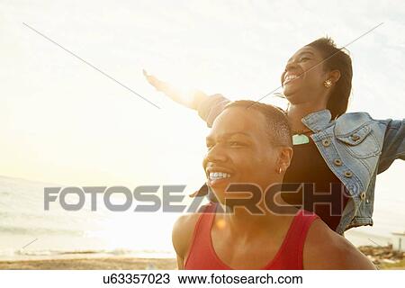 Stock Image - Young woman with arms raised standing behind young man. Fotosearch