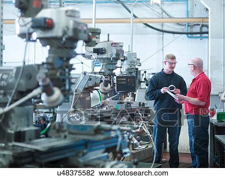 Stock Image - Apprentice engineer with instructor in engineering factory. Fotosearch