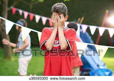 Stock Image - Boy covering his eyes for hide and seek with sister and brother in garden. Fotosearch