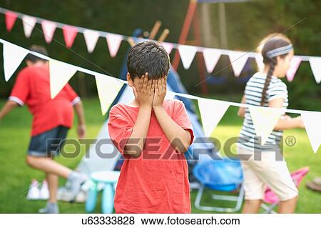 Boy covering his eyes for hide and seek with brother and sister in garden View Large Photo Image Stock Photo - Boy covering his eyes for hide and seek with brother and sister in garden. Fotosearch