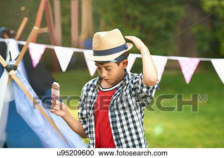 Boy eating ice lolly whilst adjusting trilby hat in garden View Large Photo Image Stock Image - Boy eating ice lolly whilst adjusting trilby hat in garden. Fotosearch