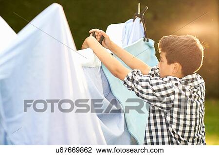 Stock Image - Boy putting bed sheets onto homemade tent in garden. Fotosearch