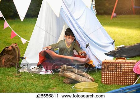 Stock Image - Boy shaking blanket from homemade tent in garden. Fotosearch