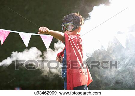 Stock Photo - Boy wearing goggles and cape in superhero stance in front of smoke cloud. Fotosearch