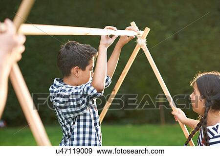 Stock Photo - Brother and sister putting up homemade tent frame in garden. Fotosearch
