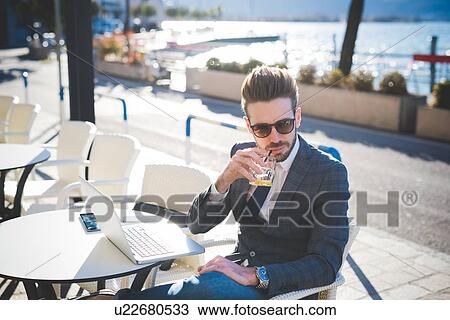 Stock Image - Businessman having a drink at lakeside cafe, Rovato, Brescia, Italy. Fotosearch