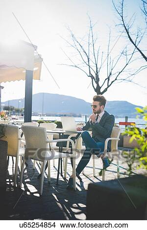 Businessman using laptop at lakeside cafe, Rovato, Brescia, Italy View Large Photo Image Picture - Businessman using laptop at lakeside cafe, Rovato, Brescia, Italy. Fotosearch