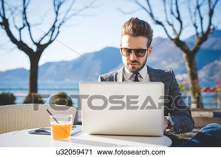 Stock Image - Businessman using laptop at lakeside cafe, Rovato, Brescia, Italy. Fotosearch