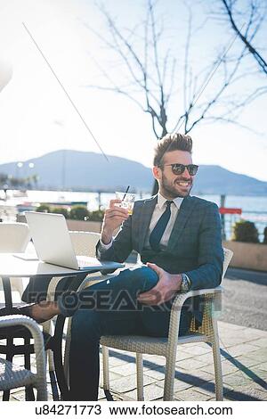 Stock Image - Businessman with laptop having a drink at lakeside cafe, Rovato, Brescia, Italy. Fotosearch
